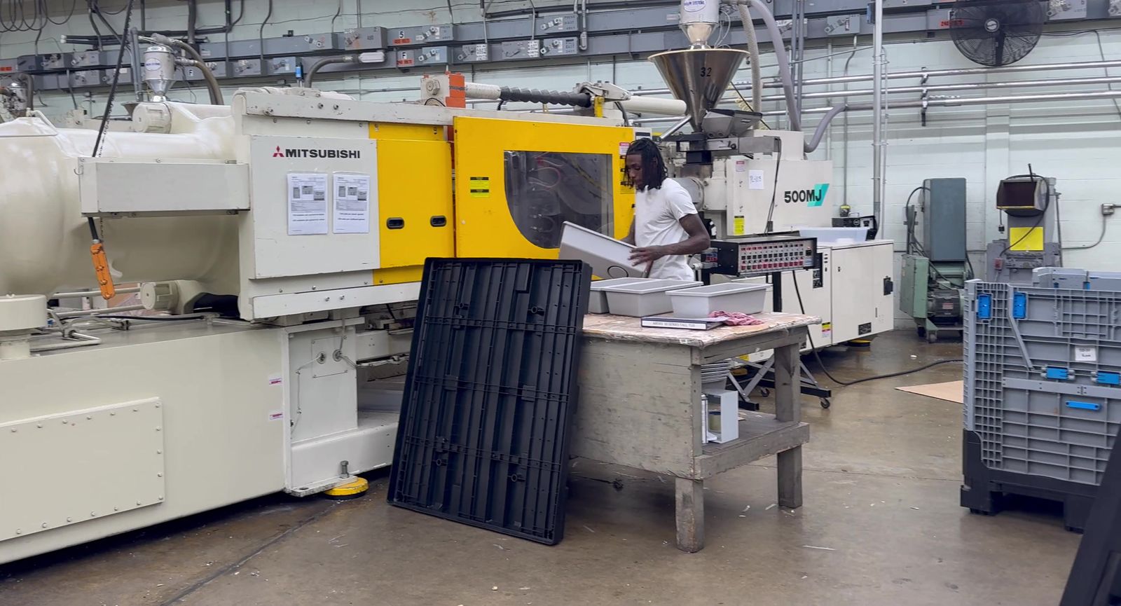 An operator working at injection molding machine 32, a white and yellow Mitsubishi, on the Burco floor