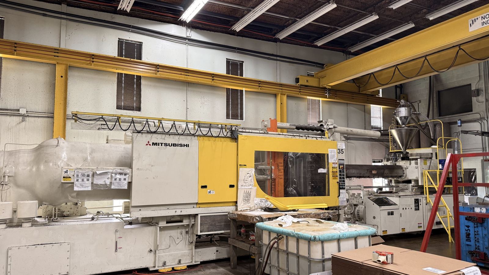 A Mitsubishi injection molding machine with its yellow guard door and hopper